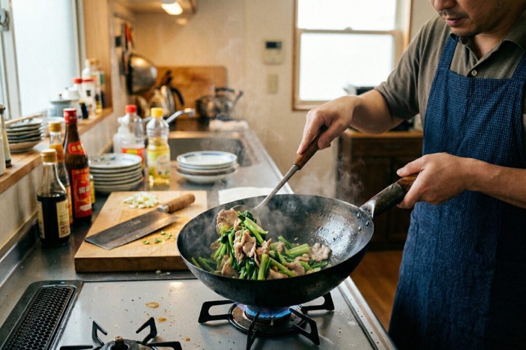 鉄の中華鍋とお玉で、青菜と肉を炒める様子