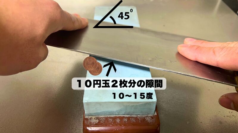 砥石に対して45度に置いた中華包丁の背に、10円玉2枚分の隙間を作って10〜15度の角度を固定している様子。
