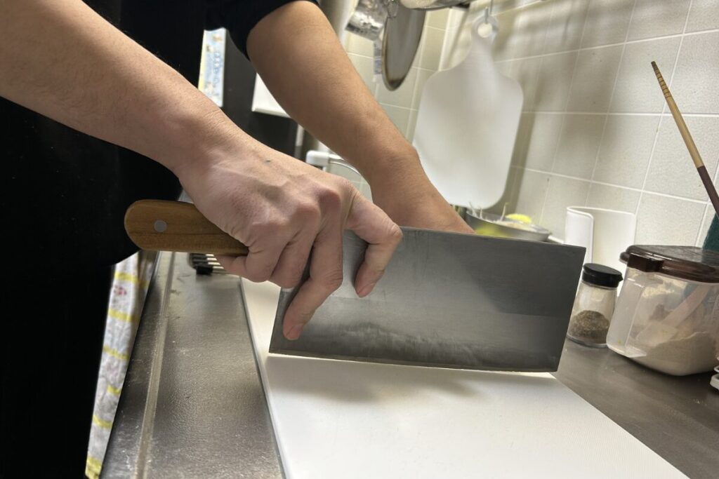 中華包丁のピンチグリップ（添え指）の持ち方。親指と人差し指で刃の根元を挟み込んでいる