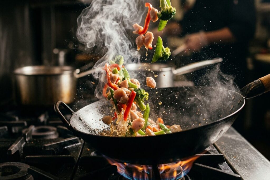 鉄の中華鍋に食材を入れて湯気が立つ様子
