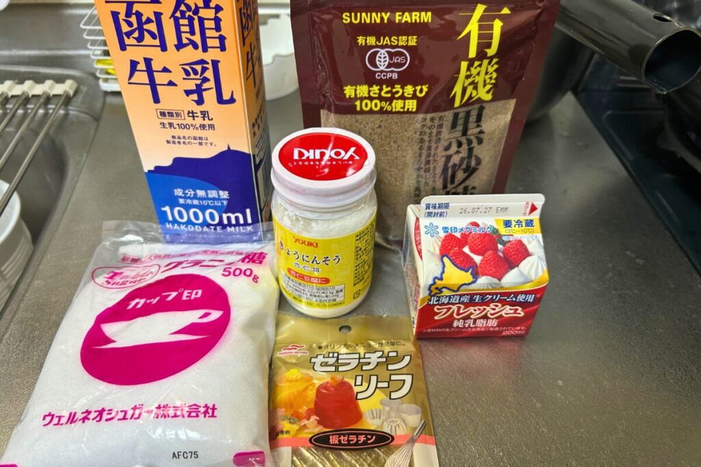 杏仁豆腐の材料一覧。牛乳・生クリーム・水・杏仁霜・黒砂糖・グラニュー糖・板ゼラチンを並べた写真