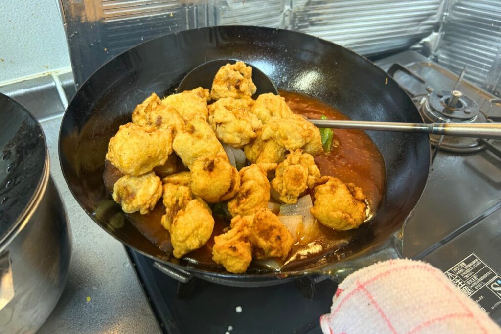 とろみをつけた甘酢あんに揚げた豚肉と野菜を戻す工程