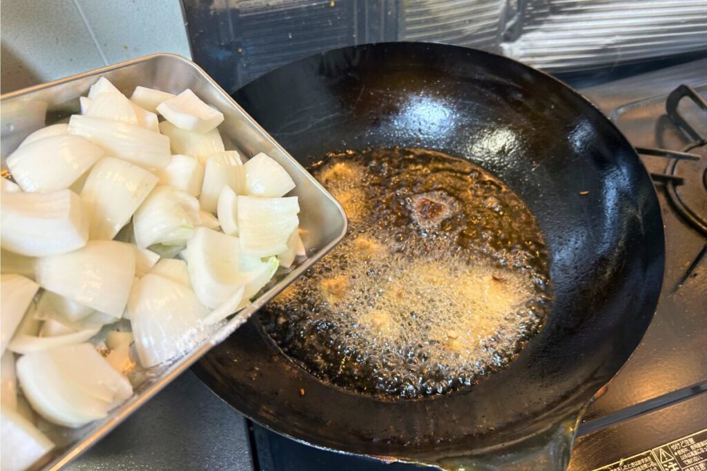 玉ねぎをバットから油に滑らせて入れる様子。透き通ってきたら次の野菜へ