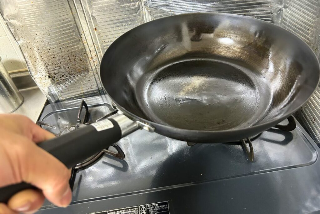 コンロに置いたニトリ鉄炒め鍋のハンドルを片手で握っている様子（30cm・約1.37kg）