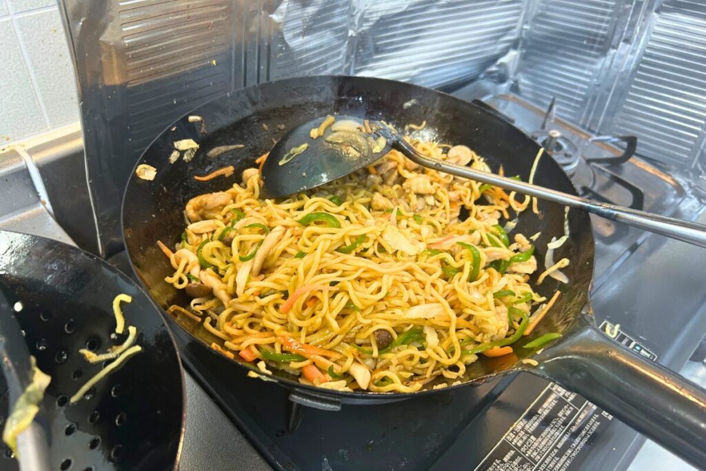 中華鍋で麺と具材にタレを絡めて和える様子
