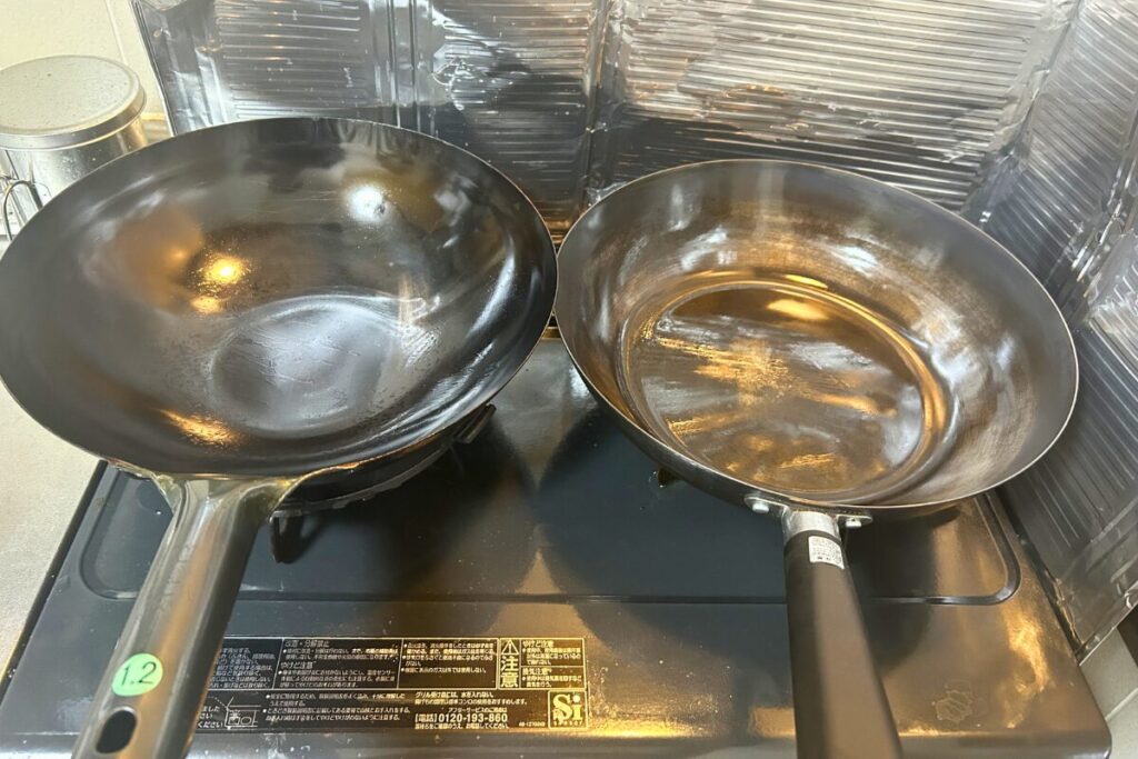 山田工業所の中華鍋30cm（左・炒飯調理後）とニトリの鉄炒め鍋30cm（右・1年使用後）をコンロ上で並べた比較