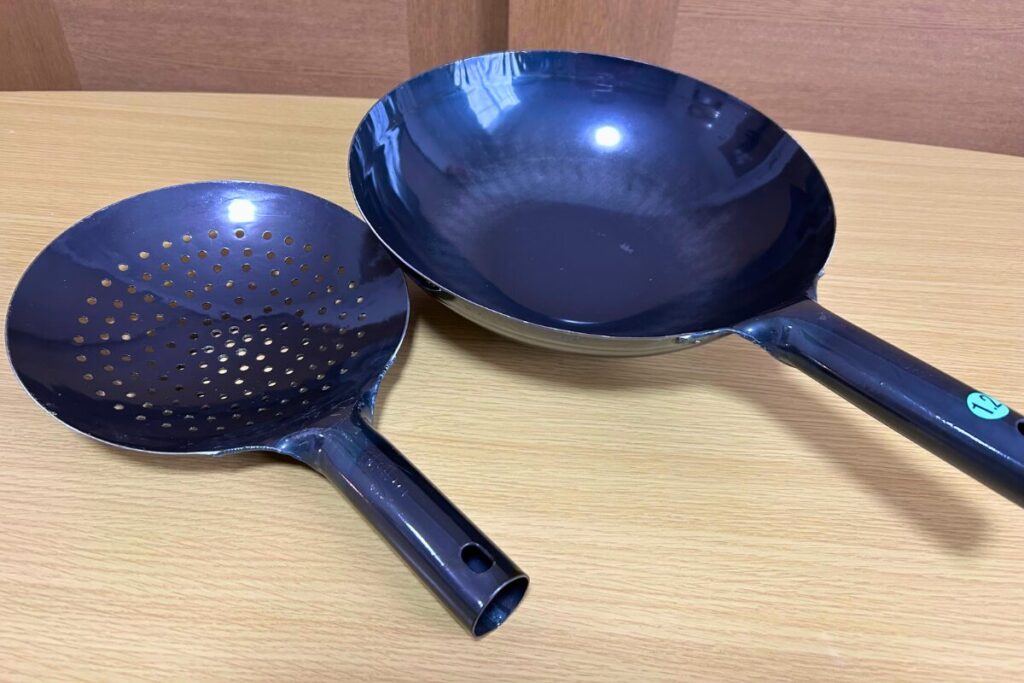 山田工業所の鉄製ザーレン21cm（新品）と山田工業所の中華鍋30cmを並べた比較。ザーレンは鍋より一回り小さい