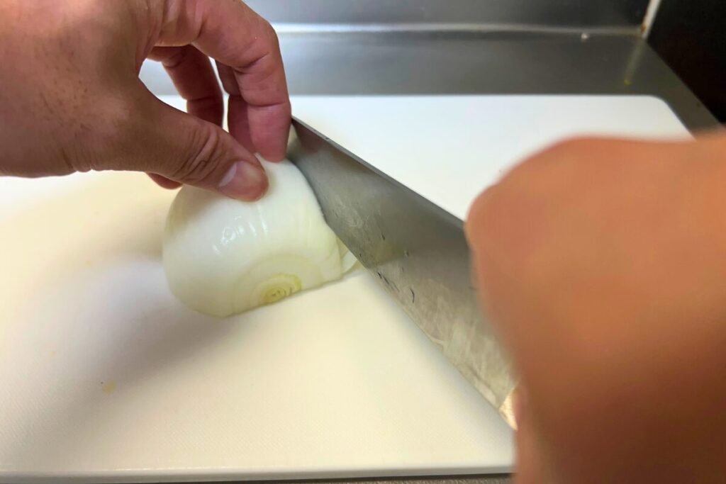 牛刀で玉ねぎを押切りする手元。刃を前に滑らせながら下ろしていく
