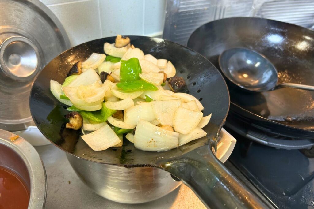 油通しした干し椎茸・玉ねぎ・ピーマンをザーレンで油切りする様子