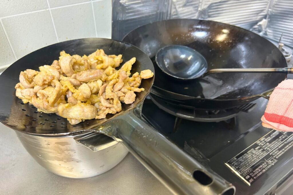 油通しした豚肉細切りをザーレンですくい上げる様子