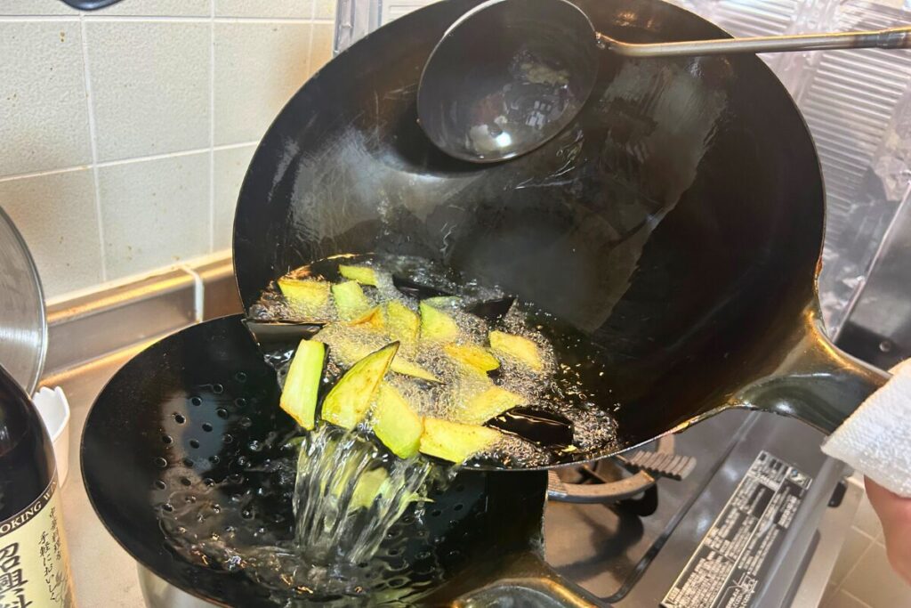 油通ししたナスをザーレンで受け、油をオイルポットへ移す様子