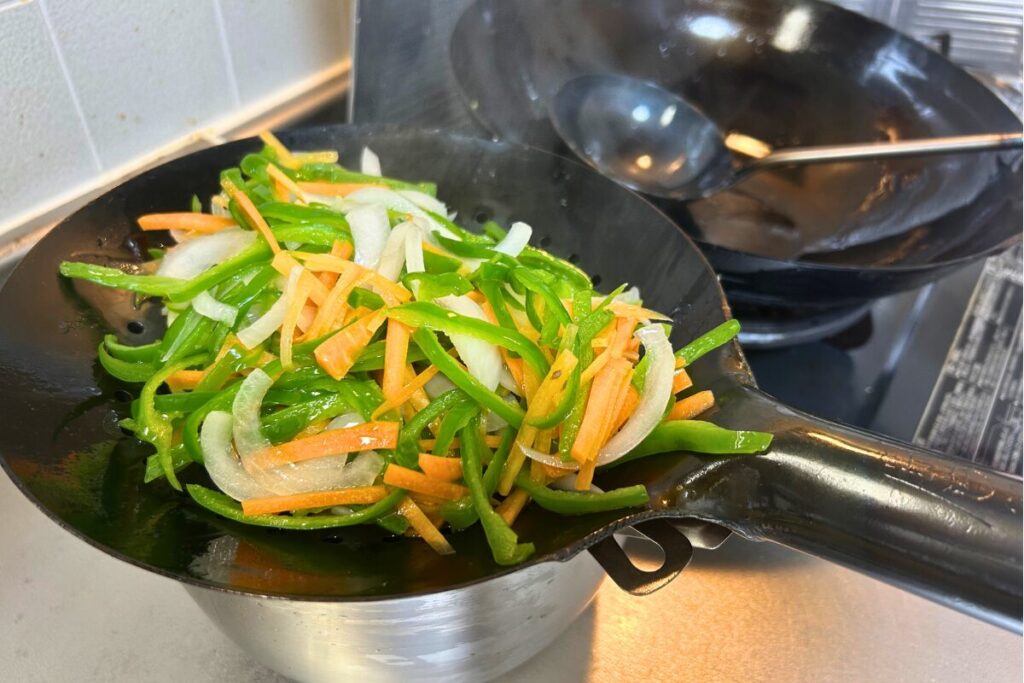 油通しした野菜をザーレンで油切りする様子