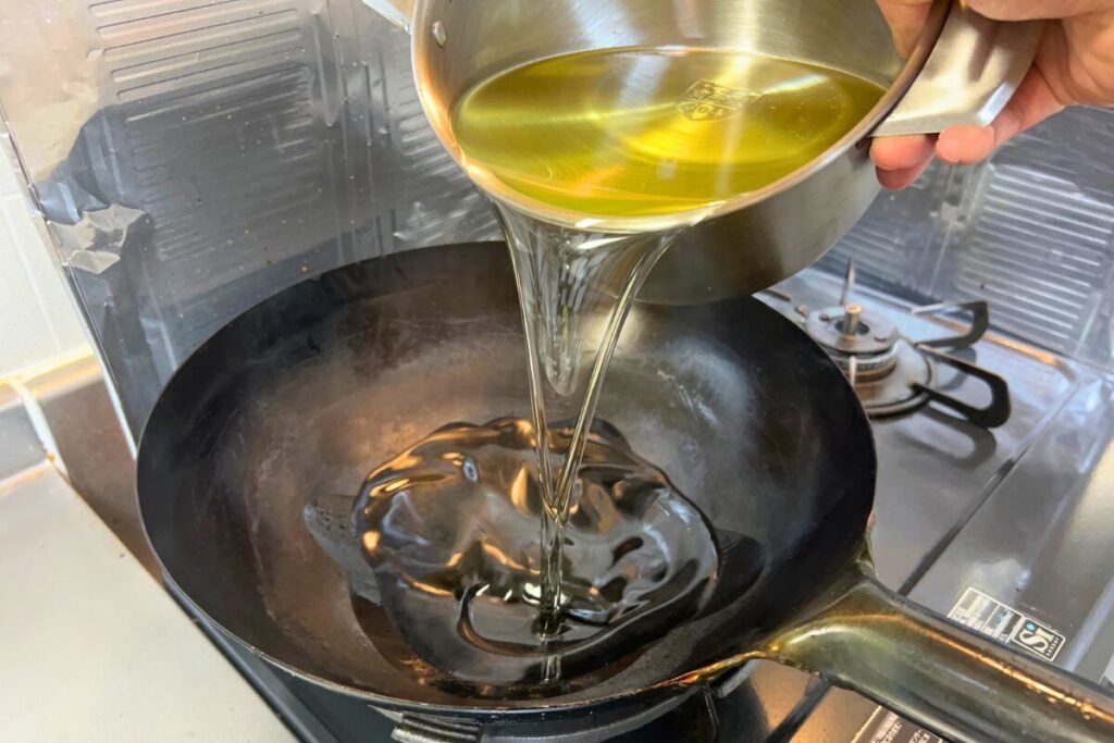 オイルポットから中華鍋へ油を注いでいる場面