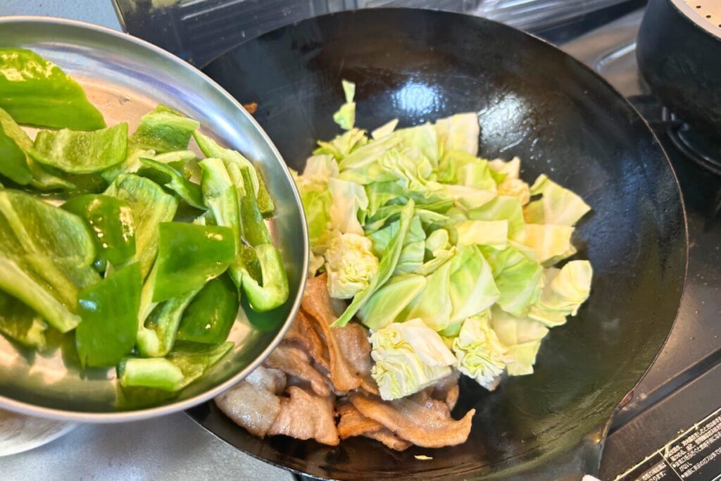 生のキャベツとピーマンを鍋に加えている様子(1/2)
