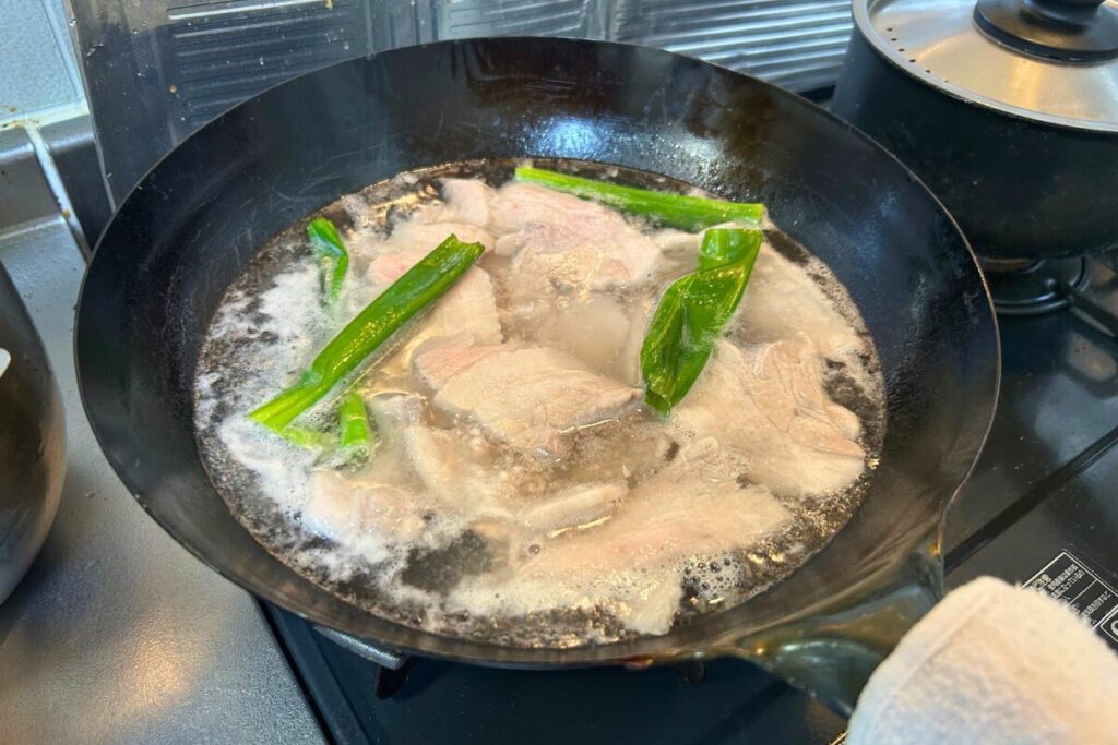 豚肉をネギとともに静かに茹でている二度調理の下ごしらえの様子
