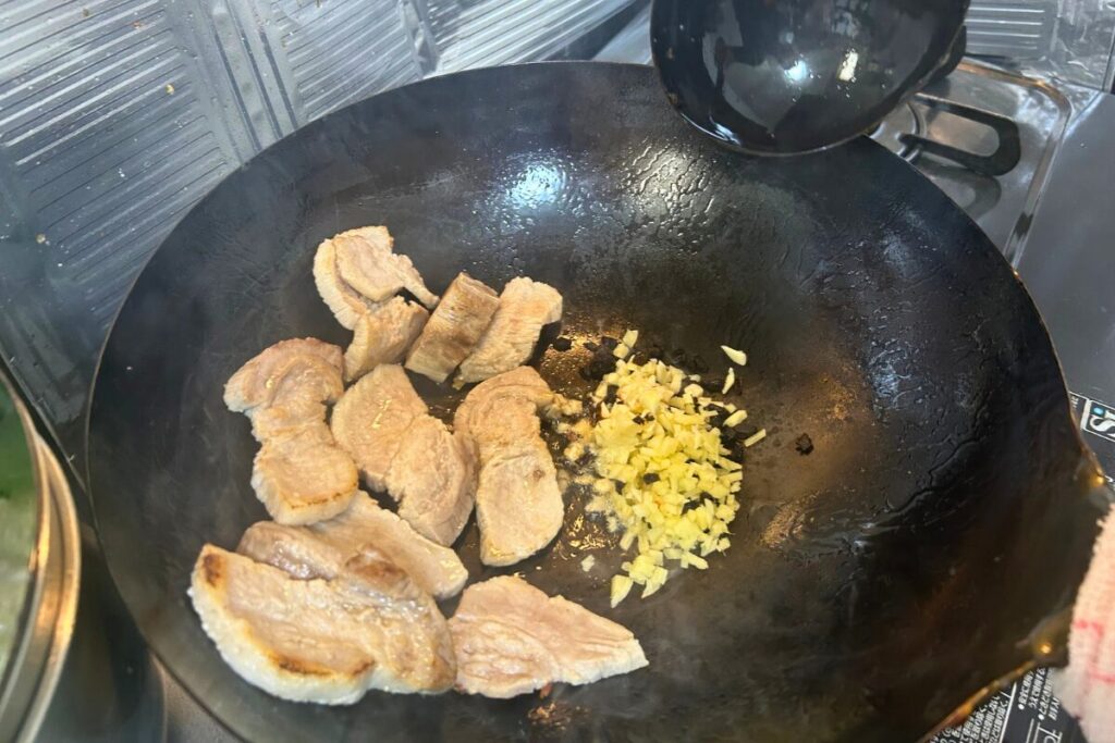 焼き色がついた豚肉を端に寄せ、空いたスペースでにんにく・生姜・豆豉・豆板醤を炒めている様子