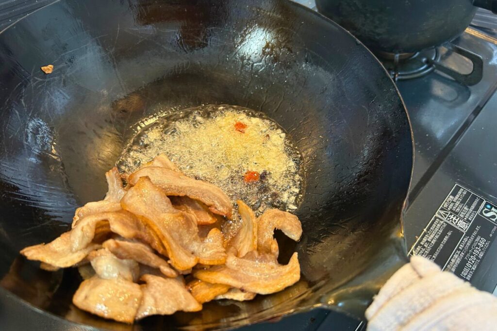 焼き色がついた豚肉を端に寄せ、空いたスペースでにんにく・豆豉・豆板醤を炒めている様子