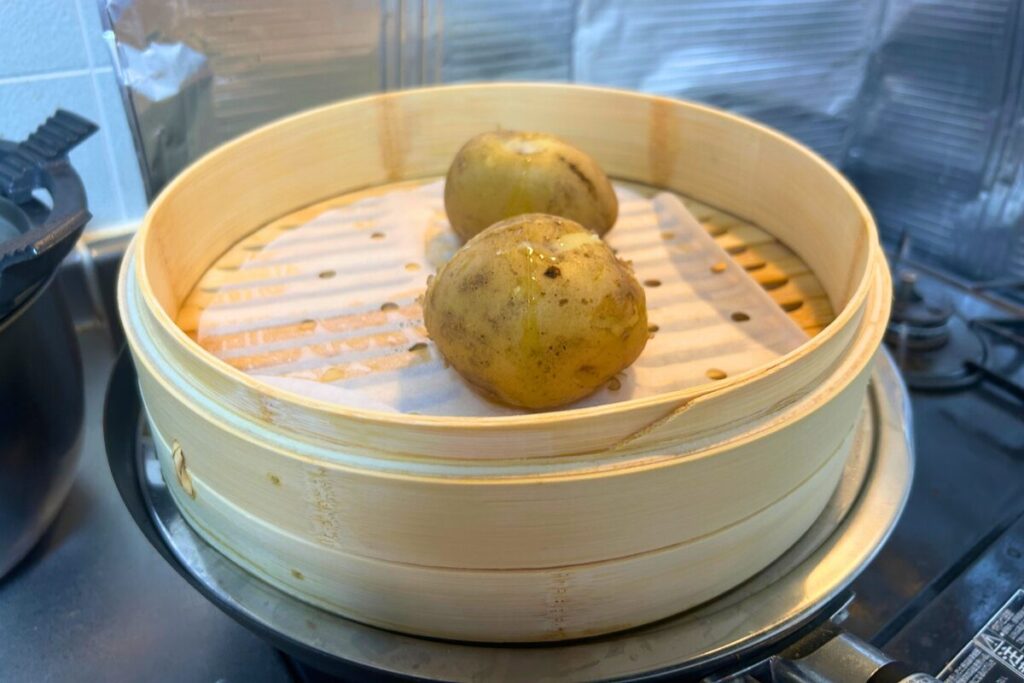 ニトリの鉄炒め鍋に蒸し板を挟んだ竹せいろで、皮つきのじゃがいもを蒸している様子