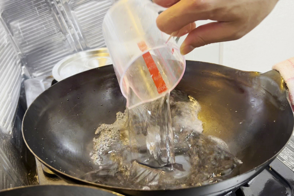 中華鍋に計量カップで水を注ぎ、スープの分量を計っているところ