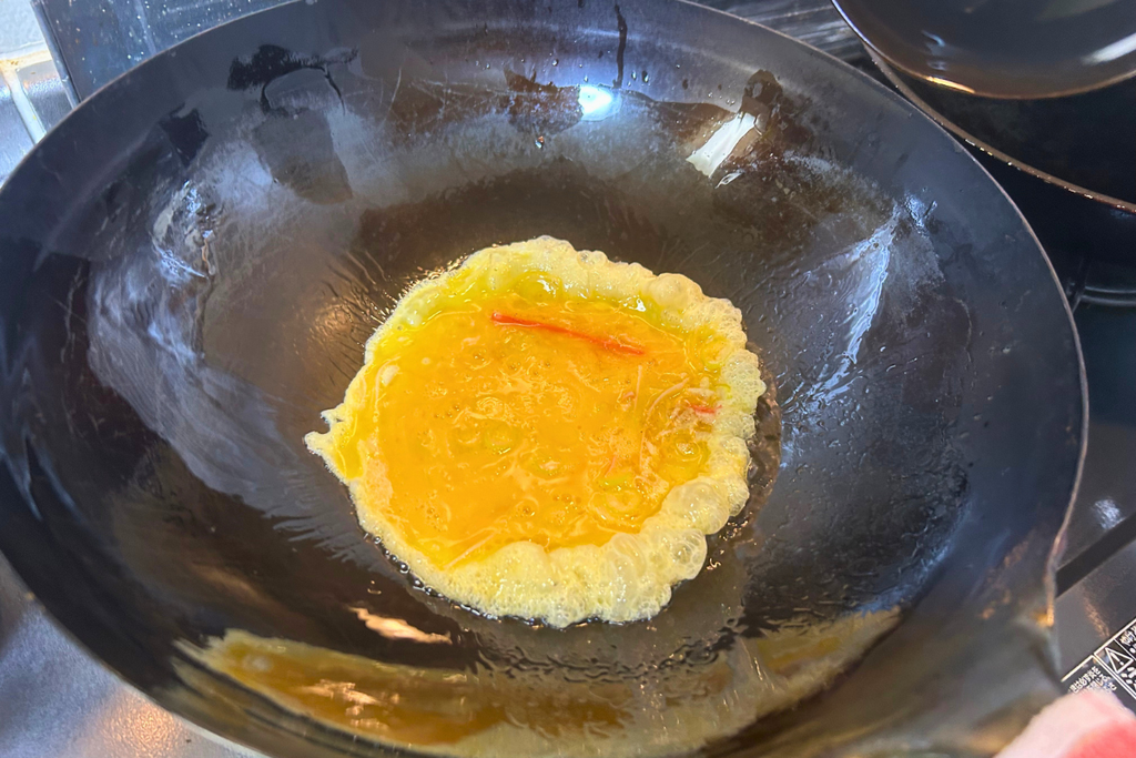 熱した中華鍋に卵液を流し入れ、縁がふくらみ始めた天津飯の卵