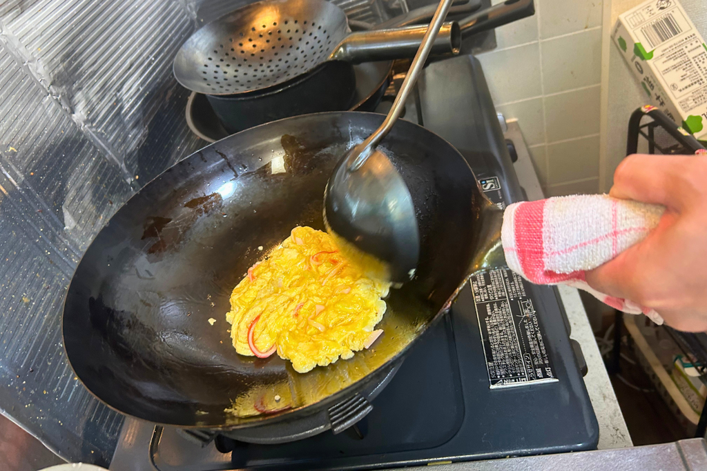 中華お玉で外側から内側へ、卵を大きくゆっくり混ぜている場面