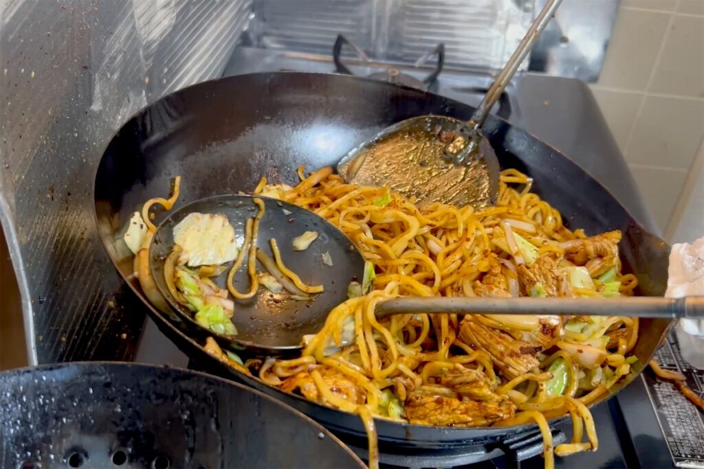 焼きそばを炒める中華鍋に入った、手前のお玉と奥の中華ヘラ