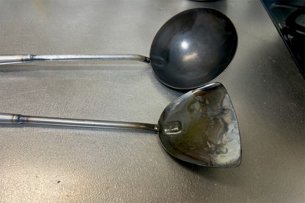鉄製の中華お玉と中華ヘラを並べたところ。お玉は丸い器、ヘラは平らな板の形