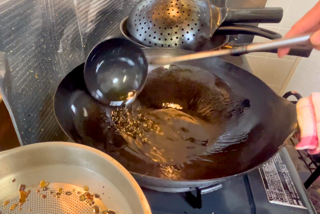 鉄の中華鍋に油を回し、お玉で鍋肌になじませる油返しの様子