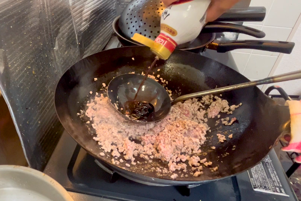 醤油・甜麺醤・砂糖をお玉にまとめ、鍋肌で合わせる様子