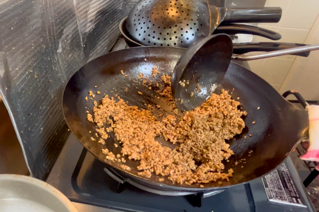 調味料を絡めた豚ひき肉を、中華鍋で水分を飛ばしながら炒めている様子