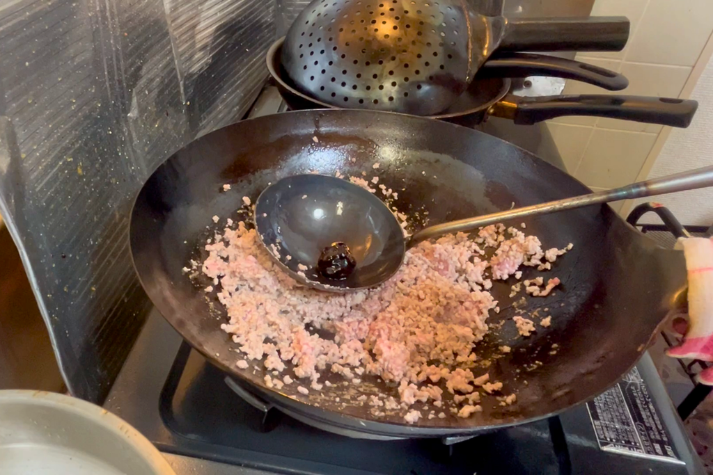 炒めた豚ひき肉の上で、お玉に甜麺醤を入れている様子