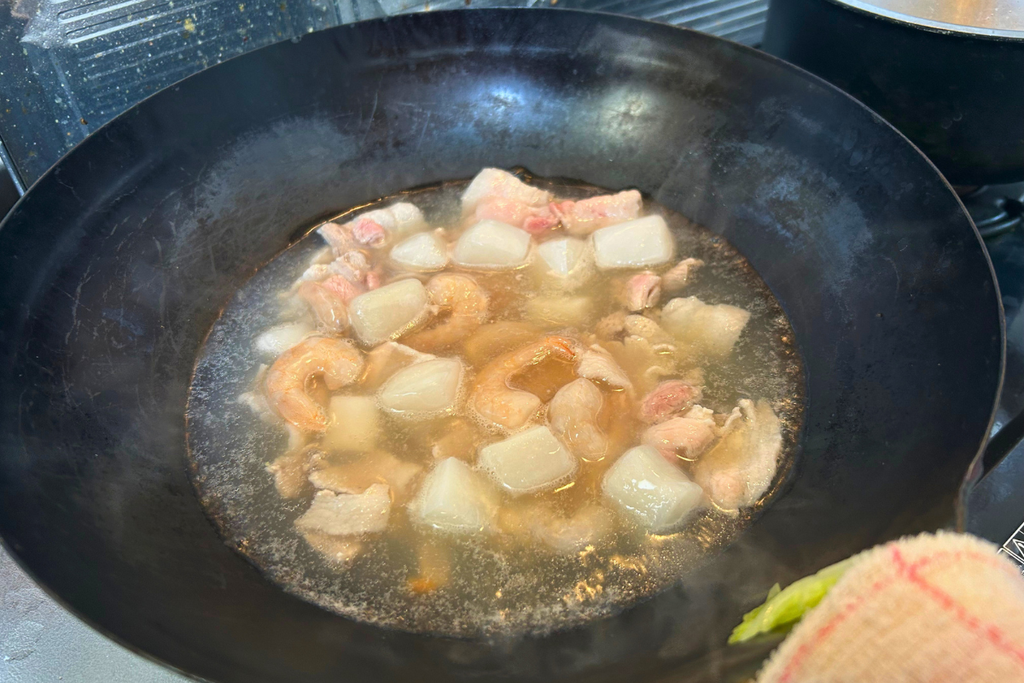 中華鍋の湯で、豚バラ肉と凍ったままのエビ・イカを煨する様子。