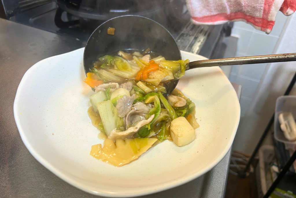 煮上がった八宝菜を、お玉で器に盛り付ける様子。