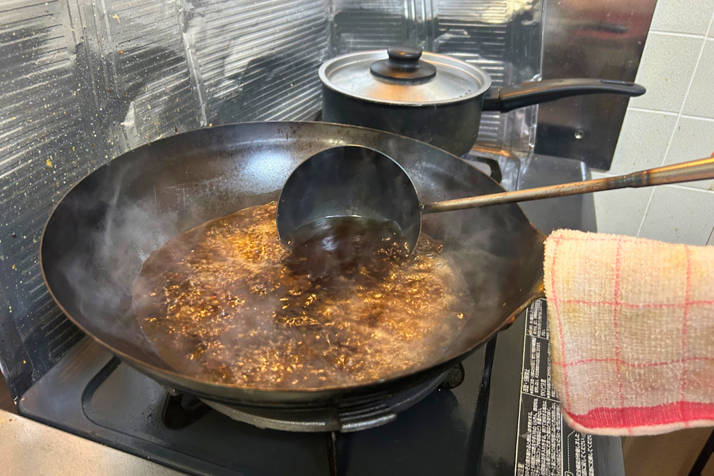 煨の湯を捨てた中華鍋で、合わせ調味料を沸かす様子。
