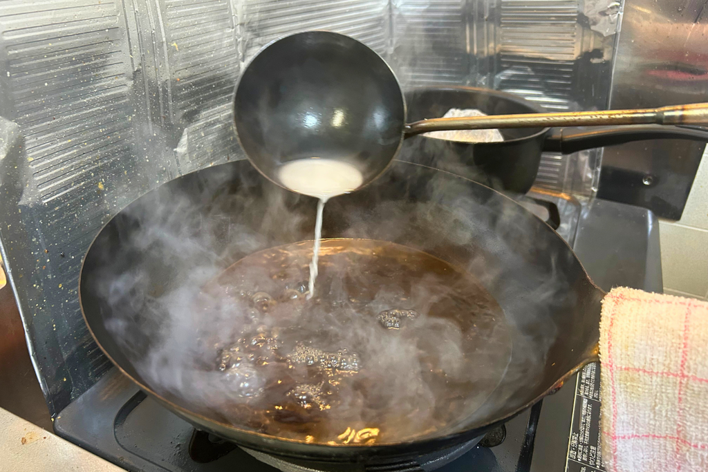 火を止めた中華鍋に、お玉から水溶き片栗粉を入れる様子。